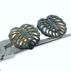 A heart-shaped black mother of pearl bead with a leaf pattern design, with a mix of dark and light brown colors.