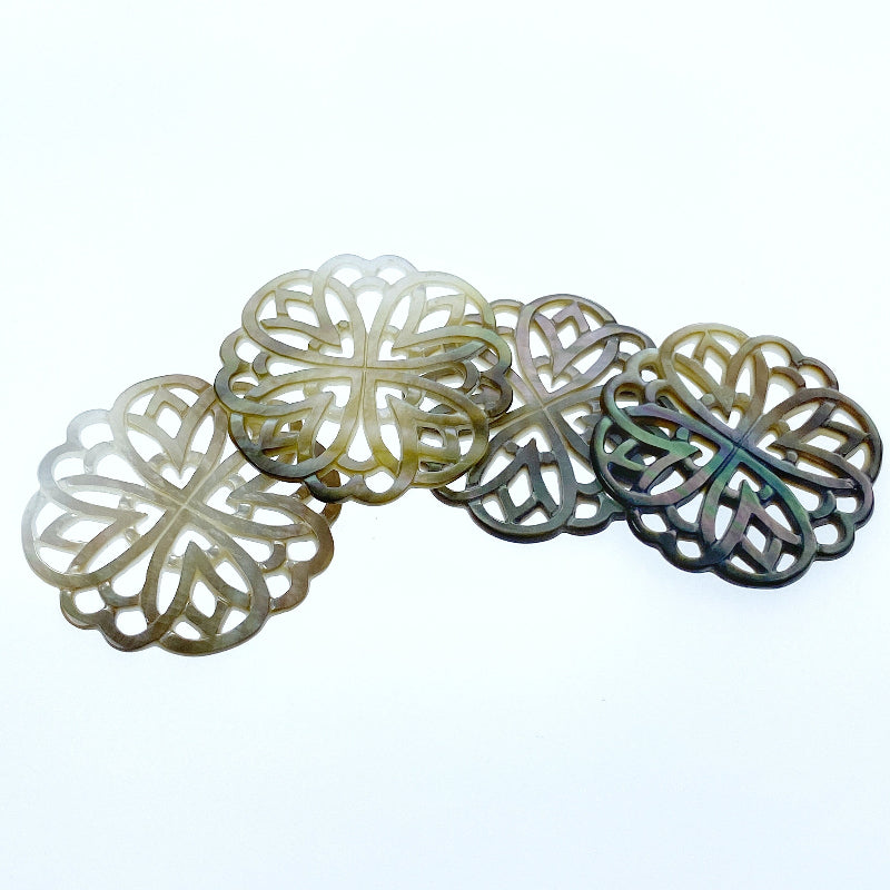 A close-up image of a round black mother of pearl filigree pendant with a metallic sheen, held by a needle.