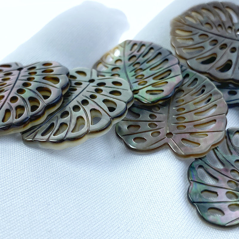 A heart-shaped black mother of pearl bead with a leaf pattern design, with a mix of dark and light brown colors.