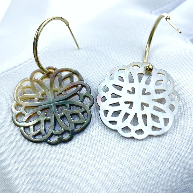 A close-up image of a round black mother of pearl filigree pendant with a metallic sheen, held by a needle.