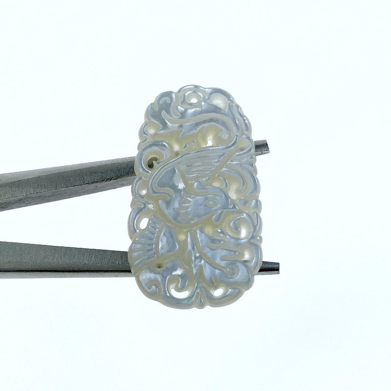 A close-up image of a hand-carved white mother of pearl pendant with a floral and phoenix pattern, attached to a metal clasp.