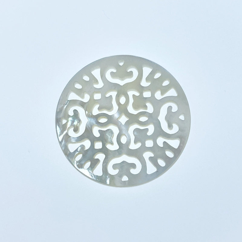 A round white mother of pearl filigree pendant on a white background.