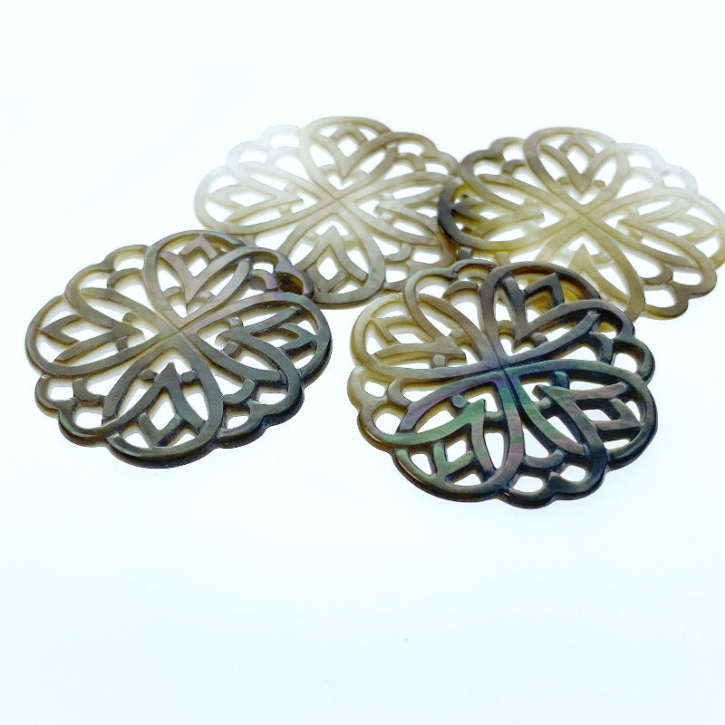 A close-up image of a round black mother of pearl filigree pendant with a metallic sheen, held by a needle.